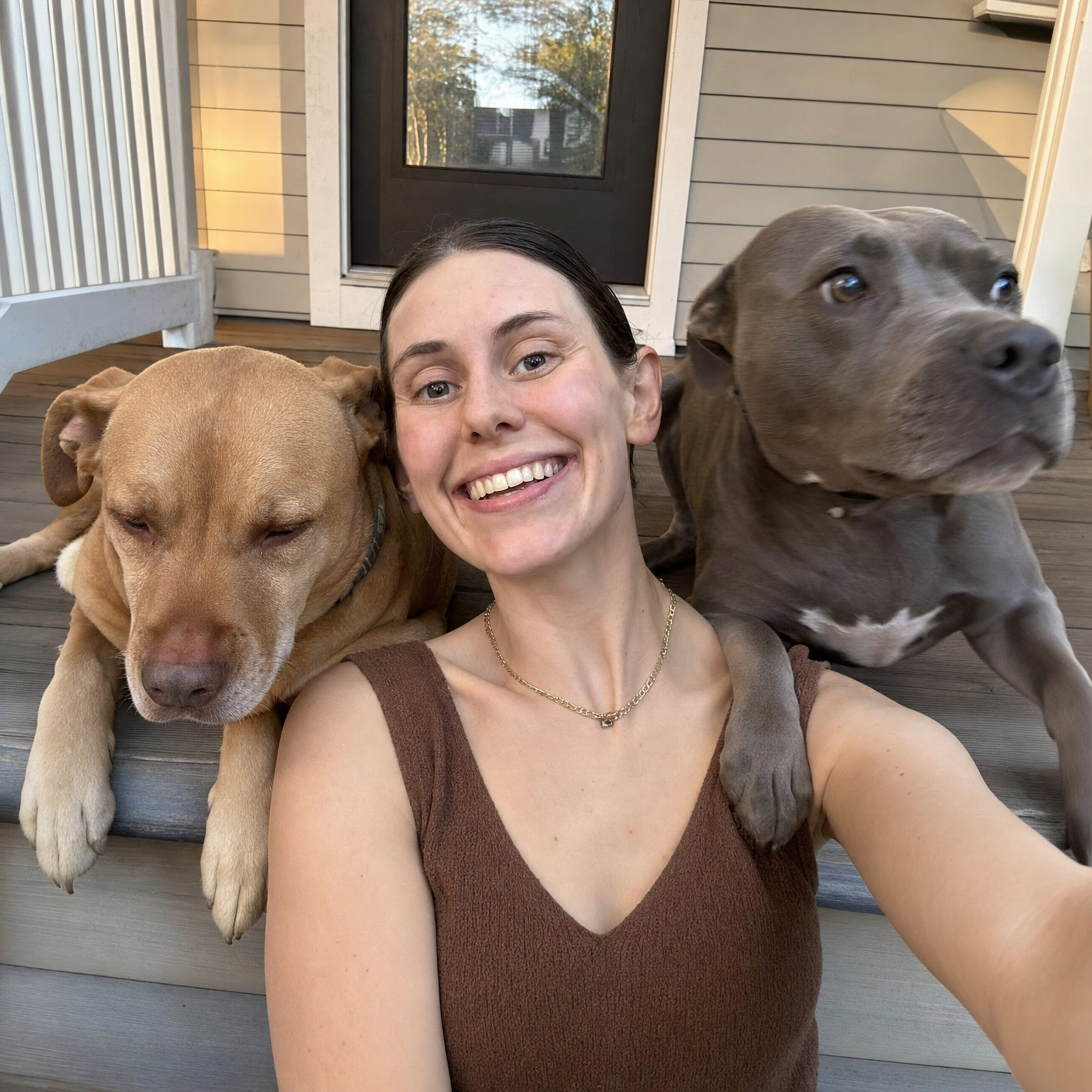 Selfie of Ellie on her front porch steps between her two pit bulls, Roger resting on the left and Ivy alert on the right